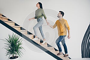 Full body profile photo of handsome guy and his pretty lady leading macho to bedroom going up stairs in modern interior