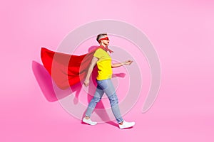 Full body profile portrait of confident superhero lady walking empty space flying cape isolated on pink color background