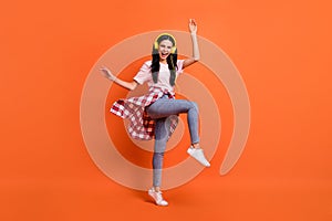 Full body profile portrait of excited pretty girl raise hands knee open mouth smile isolated on orange color background