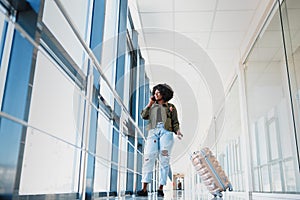 Full body profile portrait of happy female traveler walking with suitcase bag and cellphone