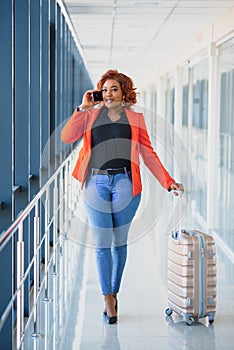Full body profile portrait of happy female traveler walking with suitcase bag and cellphone