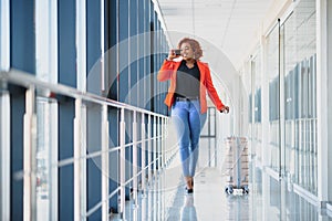 Full body profile portrait of happy female traveler walking with suitcase bag and cellphone