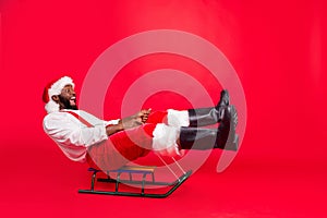 Full body profile side photo of amazed funny black santa claus riding toy sledges screaming wearing xmas pants trousers