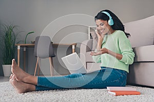 Full body profile side photoof young black woman happy smile sit floor earphones video call laptop indoors photo