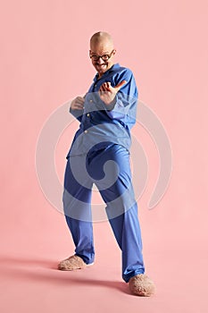 Full body shoot of funny man in pajama playing imaginary guitar over pastel rose background. photo