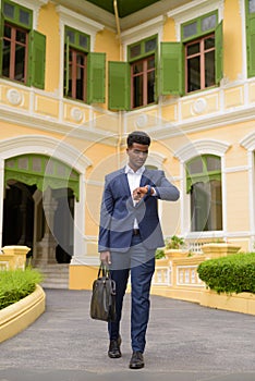 Full body shot of African businessman outdoors wearing suit while checking time from wristwatch