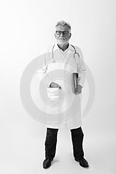 Full body shot of handsome senior bearded man doctor standing while holding clipboard against white background