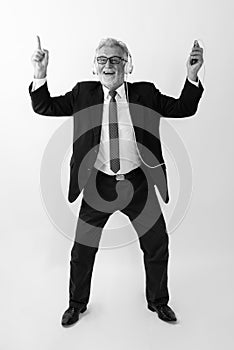 Full body shot of happy senior bearded businessman smiling while dancing and listening to music against white background