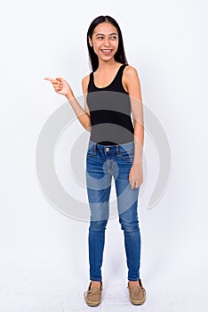 Full body shot of happy young Asian woman pointing finger