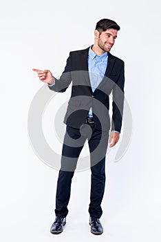 Full body shot of happy young bearded Persian businessman pointing to side and looking away