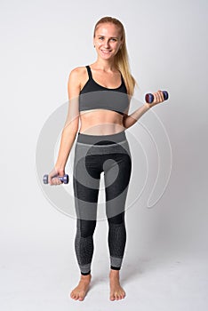 Full body shot of happy young blonde woman exercising with dumbbells ready for gym