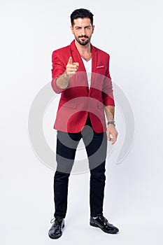 Full body shot of young handsome bearded businessman pointing at camera