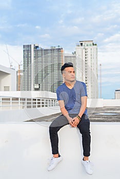 Full body shot of young handsome multi ethnic man sitting against view of the city