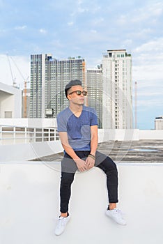 Full body shot of young handsome multi ethnic man with sunglasses sitting against view of the city