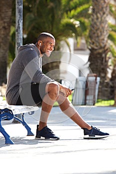 Full body portrait of fit black guy sitting on bench and listening music