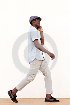 Full body side of young african man walking outside talking on phone