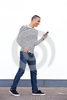Side portrait of young man walking and looking at cellphone by white wall
