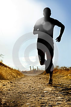 Full body silhouette of extreme cross country man running on rural track jogging at sunset
