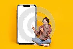 Full body size photo of young girl pointing finger empty space nomad phone touchscreen wear sweatshirt  on