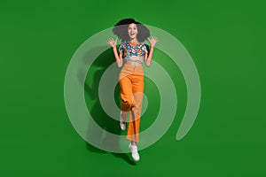 Full body size photo of young girl wear orange trousers and exotic style top raised arms up jumping isolated on green