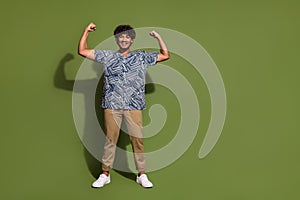 Full body size photo of young sportsman standing raised fists up showing his fit big biceps muscles isolated over khaki
