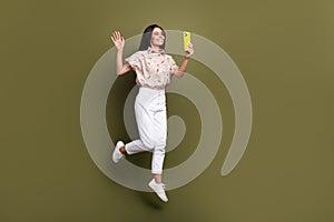 Full body size shot of woman blogger photographing selfie herself jumping with smartphone waving palm isolated on khaki