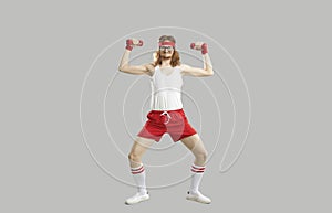 Funny skinny athlete doing fitness exercise with dumbbells isolated on gray background