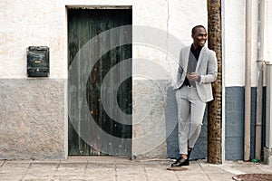 Full body smiling african american businessman standing by wall with mobile phone