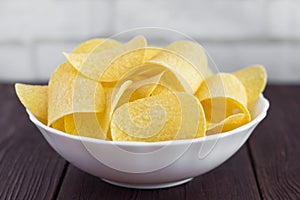 A full bowl of delicious potato chips on a wooden table,close-up