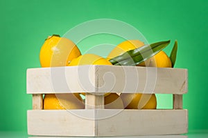 Full box of large yellow lemons close-up, on green background