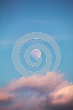Full bright moon before sunset over the clouds. With vibrant blue sky. Grainy look.