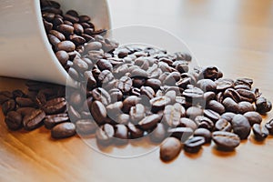 Full of coffee beans spilling out white ceramic cup on brown wooden background