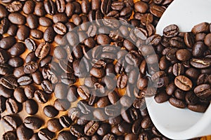 Full of coffee beans spilling out white ceramic cup on brown wooden background