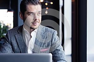 Full concentration. Good looking young man in full suit using computer while sitting in the cafe