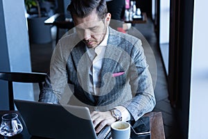 Full concentration. Good looking young man in full suit using computer while sitting in the cafe