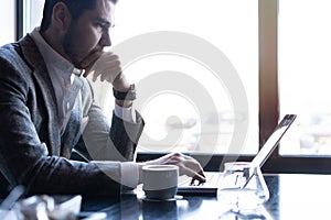 Full concentration. Good looking young man in full suit using computer while sitting in the cafe