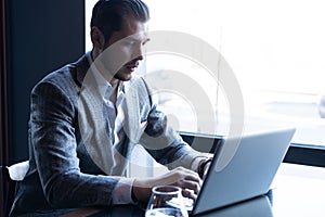 Full concentration. Good looking young man in full suit using computer while sitting in the cafe