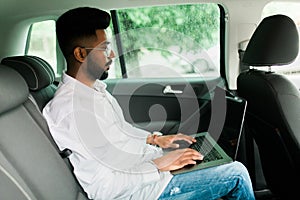 Full concentration at work. Confident indian young man in full suit working using laptop while sitting in the car