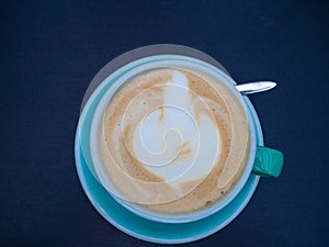 Full cup of art latte cappuccino coffee with milk froth on blue saucer isolated on trendy blue classic background, close