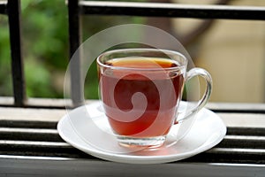 FULL CUP RED LIQUOR TEA IN TRANSPARENT IN WINDOW AS MORNING TEA