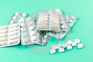 Full and empty packs of white capsules and pills packed in blisters with copy space on aquamarine background. Focus on foreground,