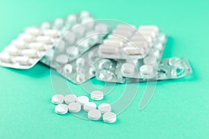 Full and empty packs of white capsules and pills packed in blisters with copy space on aquamarine background. Focus on foreground,
