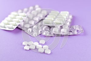 Full and empty packs of white capsules and pills packed in blisters with copy space on purple background. Focus on foreground, sof