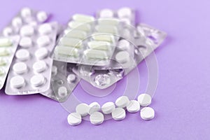 Full and empty packs of white capsules and pills packed in blisters with copy space on purple background. Focus on foreground, sof