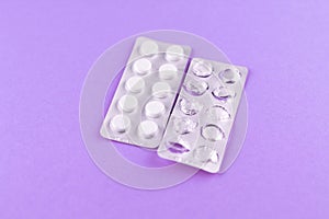 Full and empty packs of white pills packed in blisters with copy space on purple background. Focus on foreground, soft bokeh