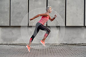 Full of energy. Side view of active middle aged woman in sport clothing jumping while exercising outdoors