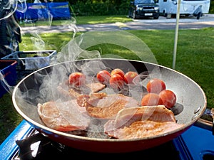 Full English breakfast cooking outside on camping site. Summer Scene.