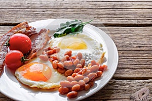 Full english breakfast with eggs, bacon, beans, tomatoes in a plate with fork on rustic wooden table. Tasty food