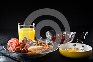 Full English breakfast with scrambled eggs in a frying pan, bacon, sausage, beans, tomatoes and juice