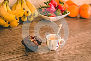 Full espresso cup and a chocolate muffin on top of a wooden table